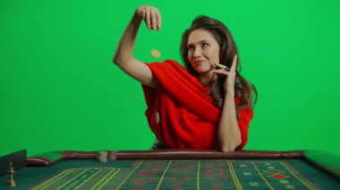 Kumarhane ve kumar yaratıcı reklam konsepti. Krom anahtar yeşil ekran yakından çekilmiş kadın portresi. Rulet masasında kırmızı elbiseli zarif bir kadın cips fırlatıyor ve gülümsüyor. Yavaş çekim.
