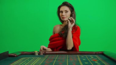 Kumarhane ve kumar yaratıcı reklam konsepti. Krom anahtar yeşil ekran yakın çekim üzerinde çekici bir kadın portresi. Rulet masasında kırmızı elbiseli bir kadın, kameraya şakacı poz veriyor..