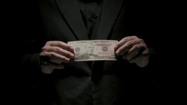 İş ve para yaratıcı reklam konsepti. Düşük ışıkta siyah arka planda izole edilmiş siyah elbiseli kadın portresi. Elinde elli dolarlık banknot tutan kadın kameraya bakıyor..