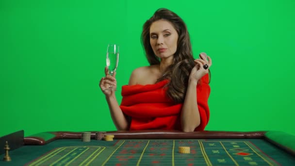 カジノとギャンブルクリエイティブ広告コンセプト クロマキーグリーンクローズショットの魅力的な女性の肖像画 ルーレットテーブルドリンクの赤いドレスの女性 シャンパンは賭けるためにチップを保持します — ストック動画