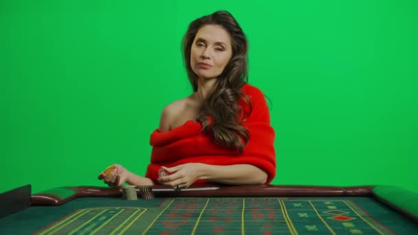 カジノとギャンブルクリエイティブ広告コンセプト クロマキーグリーンクローズショットの魅力的な女性の肖像画 ルーレットテーブルの赤いドレスの女性は カメラで微笑むチップを保持しています — ストック動画