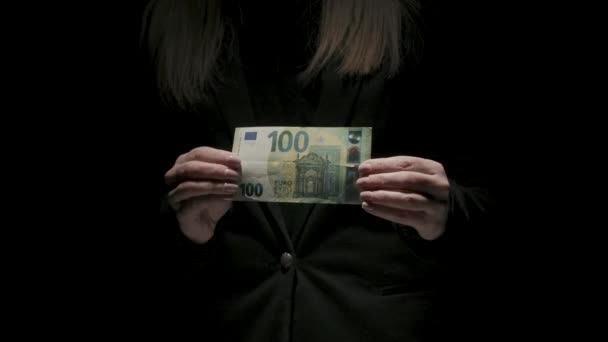 商业和货币创意广告的概念 穿着黑色西服的女性画像 背景为黑色 光线昏暗 手里拿着100欧元钞票的女人斜着身子站在摄像机旁边 — 图库视频影像
