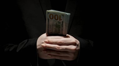 İş ve para yaratıcı reklam konsepti. Düşük ışıkta siyah arka planda izole edilmiş siyah elbiseli kadın portresi. Elinde bir tomar para tutan bir kadın..