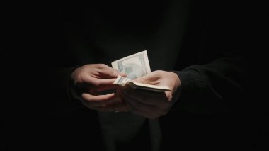 İş ve para yaratıcı reklam konsepti. Düşük ışıkta siyah arka planda izole edilmiş siyah elbiseli erkek portresi. Elinde bir tomar para tutan ve notlar sayan bir adam..