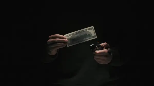 商业和货币创意广告的概念 穿着黑色衣服的男性画像 背景为黑色 光线昏暗 男人拿着100美元的钞票 点着打火机 — 图库照片