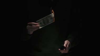 İş ve para yaratıcı reklam konsepti. Düşük ışıkta siyah arka planda izole edilmiş siyah elbiseli erkek portresi. Elinde 100 dolarlık banknot tutan adam çakmağı yakıp parayı yakıyor..