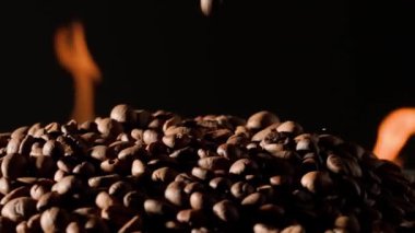 Kahve çekirdekleri alevler içinde yanan dillerle siyah bir stüdyonun arka planında dönüyorlar. Canlandırıcı bir içki yapmak için kahve pişirme süreci. Kahve dükkanı veya restoran reklamı konsepti