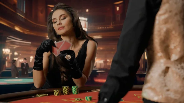 在赌场玩二十一点游戏时 穿着黑色衣服的迷人女人坐在扑克牌桌旁 拿着扑克牌的女人正在考虑她的举动赌场和赌博的概念 — 图库照片