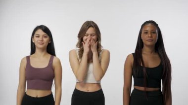 Doğal güzellik ve çeşitlilik reklam konsepti. Beyaz stüdyo arka planında çok ırklı genç modellerin portresi yakın plan. Üç tane çok ırklı kız ciddi poz vermeye çalışıyor ama gülüyorlar.