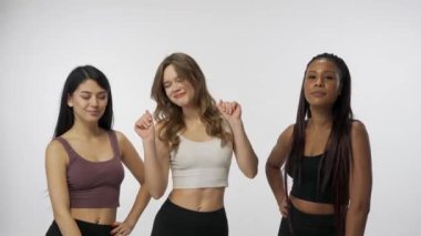 Doğal güzellik ve çeşitlilik reklam konsepti. Beyaz stüdyo arka planında çok ırklı genç modellerin portresi yakın plan. Üç güzel çok ırklı kız grubu kameraya doğru komik bir şekilde dans ediyor.