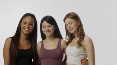 Doğal güzellik ve çeşitlilik reklam konsepti. Beyaz arka planda izole edilmiş çok ırklı modellerin portresi, yakın çekim. Üç tane çok ırklı genç kız fotoğraf makinesinin önünde birbirine sarılıyor.