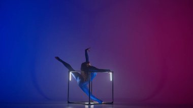 Modern koreografi ve akrobasi yaratıcı reklam konsepti. Kadın akrobatın silueti neon arka planda izole edildi. Mavi, ışıl ışıl vücutlu kadın jimnastik dansçısı küpte parçalanmış..