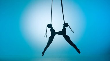Modern koreografi ve akrobasi yaratıcı reklam konsepti. Mavi neon arka planda izole edilmiş iki kadın akrobatın silueti. Kızların dansçıları iplerle akrobatik uçuşlar yapıyorlar..