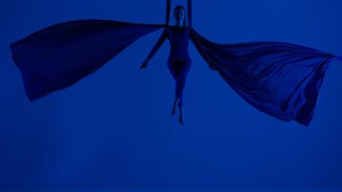 Modern koreografi ve akrobasi yaratıcı reklam konsepti. Mavi neon stüdyo arka planında izole edilmiş kadın sanatçı silueti. Kız dansçı hava ipeği üzerinde süzülüyor..