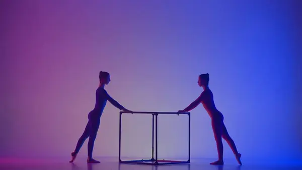 現代の振付とアクロバットクリエイティブ広告コンセプト ネオンの鮮やかな背景に隔離された2人の女性のアクロバットのシルエット キューブでアクロバティックな要素を実行する少女の体操ダンサー — ストック写真