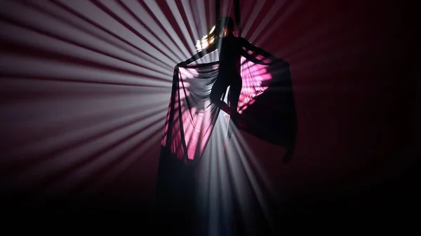 現代の振付とアクロバットクリエイティブ広告コンセプト 明るいスポットライトに対して黒い背景に隔離された女性のシルエット エアシルクでエレメントを実行する少女空中ダンサー — ストック写真