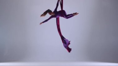 Modern koreografi ve akrobasi yaratıcı reklam konsepti. Stüdyoda beyaz arka planda izole edilmiş kadın akrobatın portresi. Kız dansçı hava ipeği üzerinde hızlı dönüş elementi sergiliyor.