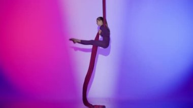 Modern koreografi ve akrobasi yaratıcı reklam konsepti. Pembe neon arka planda izole edilmiş kadın akrobat portresi. Kız hava dansçısı hava ipeğiyle ters takla atıyor..