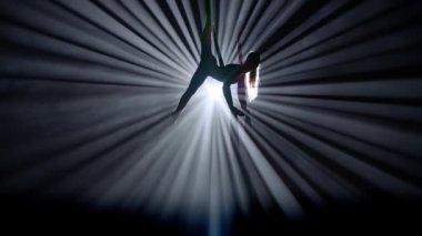 Modern koreografi ve akrobasi yaratıcı reklam konsepti. Siyah arka planda izole edilmiş, parlak spot ışığı olan bir kadın silueti. Kız hava dansçısı hava ipeğiyle dengede duruyor..