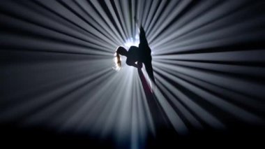 Modern koreografi ve akrobasi yaratıcı reklam konsepti. Parlak spot ışıklarına karşı siyah arkaplanda izole edilmiş bir kadın silueti. Hava ipeğinde dans eden kız..