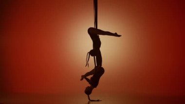 Modern koreografi ve akrobasi yaratıcı reklam konsepti. Turuncu neon arka planda izole edilmiş iki kadın akrobatın silueti. Kızlar hava dansçıları iplerde akrobatik bölünmeler yapıyorlar..