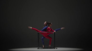 Modern koreografi ve akrobasi yaratıcı reklam konsepti. Siyah arka planda izole edilmiş iki kadın akrobatın portresi. Mavi takım elbiseli kızlar bir küpte element gösteriyorlar..