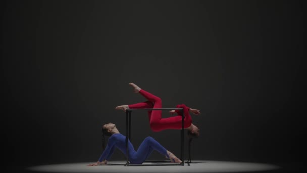 現代の振付とアクロバットクリエイティブ広告コンセプト 黒い背景に隔離された2人の女性のアクロバットの肖像画 青い赤いスーツの少女空中ダンサーは キューブ上の要素を示しています — ストック動画