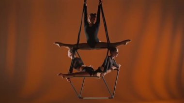 Modern koreografi ve akrobasi yaratıcı reklam konsepti. Turuncu arka planda izole edilmiş kadın akrobatların portresi. Kız akrobatlar, dansçılar üçlüsü havada iplerle dönüyor..