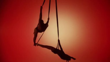Modern koreografi ve akrobasi yaratıcı reklam konsepti. Turuncu neon arka planda izole edilmiş iki kadın akrobatın silueti. Kızlar ikilisi hava dansçıları iplerde farklı elementler sergiliyor..