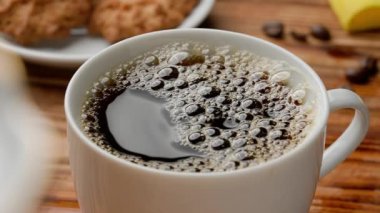 Taze demlenmiş kahve ve köpük köpüklü beyaz seramik bardak. Şeker parçaları masanın üzerinde duran fincana düşer ve su sıçratır. Sabah ritüeli, kahvaltı konsepti. Yaklaş Yavaş