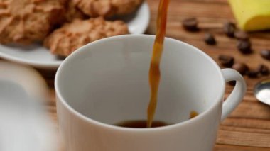 Taze demlenmiş kahve masanın üzerinde duran beyaz bir fincana dökülüyor. Kahverengi kahve ya da çay fincanı doldurur ve su kabarcıkları oluşturur. Sabah ritüeli, kahvaltı konsepti. Yaklaş Yavaş