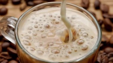 Bir süt jeti kahve fincanına dökülür ve yüzeyde köpüklerle köpük oluşturur. Makro bardak kahve ya da mutfak masasında çay fincanı. Sabah ritüeli, kahvaltı kavramı. Üst Görünüm Yavaş