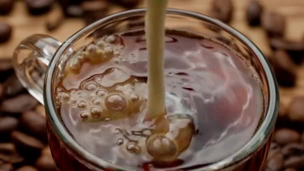 ミルクの流れが一杯のコーヒーに注ぎ込まれ そこに溶け込む マクロはキッチンテーブルにガラスコーヒーやティーカップを撮影した 朝の儀式 朝食のコンセプト トップビュー スローモーション — ストック動画