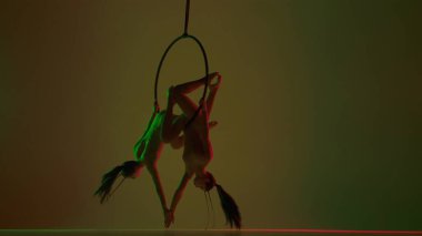 Modern koreografi ve akrobasi yaratıcı reklam konsepti. İki kadın jimnastikçi sarı stüdyo arka planında izole edilmiş. Kız dansçıları başlarını halkalara bağlayıp dönerler..