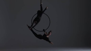 Modern koreografi ve akrobasi yaratıcı reklam konsepti. Gri stüdyo arka planında iki kadın jimnastikçi var. Havadan dansçılar halkada statik akrobatik elementler gösteriyorlar..