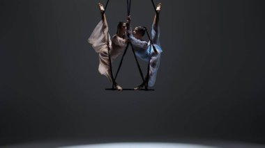 Modern koreografi ve akrobasi yaratıcı reklam konsepti. Kadın jimnastik ikilisi monokrom stüdyosunda izole edilmiş. Kızlar hava dansçıları kayışlarla akrobatik trapezde dönüyorlar..