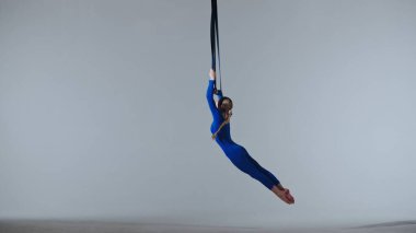 Modern koreografi ve akrobasi yaratıcı reklam konsepti. Beyaz stüdyo arka planında izole edilmiş kadın jimnastikçi. Kız hava dansçısı jimnastik kayışları üzerinde dönüyor, dans öğelerini gösteriyor.