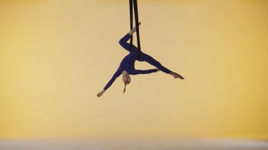 Modern koreografi ve akrobasi yaratıcı reklam konsepti. Sarı stüdyo arka planında izole edilmiş kadın jimnastikçi. Kız dansçı jimnastik kayışları üzerinde dönüyor, akrobatik öğeler gösteriyor..