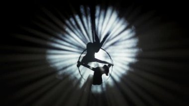 Modern koreografi ve akrobasi yaratıcı reklam konsepti. İki kadın jimnastikçi sahne ışıkları ve dumanla siyah arka planda izole edilmiş. Hava dansçıları yüzükteki elementi kayışlarla gösteriyorlar.