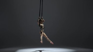 Modern koreografi ve akrobasi yaratıcı reklam konsepti. Kadın jimnastikçi monokrom stüdyosunda izole edilmiş. Akrobatik trapezdeki kız dansçı. Kayışları ikiye bölünmüş..