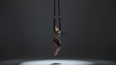 Modern koreografi ve akrobasi yaratıcı reklam konsepti. Kadın jimnastikçi monokrom stüdyosunda izole edilmiş. Akrobatik trapezdeki kız dansçı kız. Kayışlar üzerinde dönüyor..