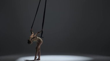 Modern koreografi ve akrobasi yaratıcı reklam konsepti. Kadın jimnastikçi monokrom stüdyosunda izole edilmiş. Akrobatik trapezde kız dansçı. Kayışlar ters takla atıyor..