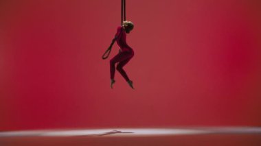 Modern koreografi ve akrobasi yaratıcı reklam konsepti. Kırmızı stüdyo arka planında izole edilmiş kadın jimnastikçi. Kız dansçı akrobat uzun kayışlarla jimnastik yapıyor..