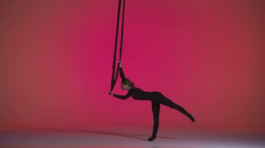 Modern koreografi ve akrobasi yaratıcı reklam konsepti. Pembe neon stüdyo arka planında izole edilmiş kadın jimnastikçi. Kız dansçı kız trapezde kemerlerle yerde duruyor.