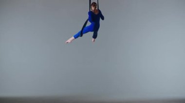 Modern koreografi ve akrobasi yaratıcı reklam konsepti. Beyaz stüdyo arka planında izole edilmiş kadın jimnastikçi. Kız hava dansçısı jimnastik kayışları üzerinde dönüyor, dans öğelerini gösteriyor.