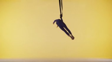 Modern koreografi ve akrobasi yaratıcı reklam konsepti. Sarı stüdyo arka planında izole edilmiş kadın jimnastikçi. Kız dansçı jimnastik kayışları üzerinde dönüyor, akrobatik öğeler gösteriyor..