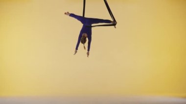 Modern koreografi ve akrobasi yaratıcı reklam konsepti. Sarı stüdyo arka planında izole edilmiş kadın jimnastikçi. Kız dansçı jimnastik kayışlarında dönüyor, parçalanmış elementler gösteriyor..