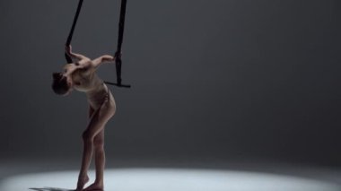 Modern koreografi ve akrobasi yaratıcı reklam konsepti. Kadın jimnastikçi, tek renkli stüdyo geçmişine sahip. Yakından çekilen dansçı kız kayışlarla akrobatik trapezde uçuyor..