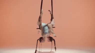 Modern koreografi ve akrobasi yaratıcı reklam konsepti. Kadın jimnastik düeti şeftali stüdyosunun arka planında izole edilmiş. Kız dansçılar başlarını jimnastik trapezine bağlı olarak eğiyorlar..