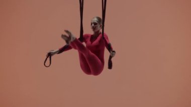 Modern koreografi ve akrobasi yaratıcı reklam konsepti. Turuncu stüdyo arka planında izole edilmiş kadın jimnastikçi. Kız dansçı jimnastik kayışlarıyla trapezde asılı, yakın çekim..